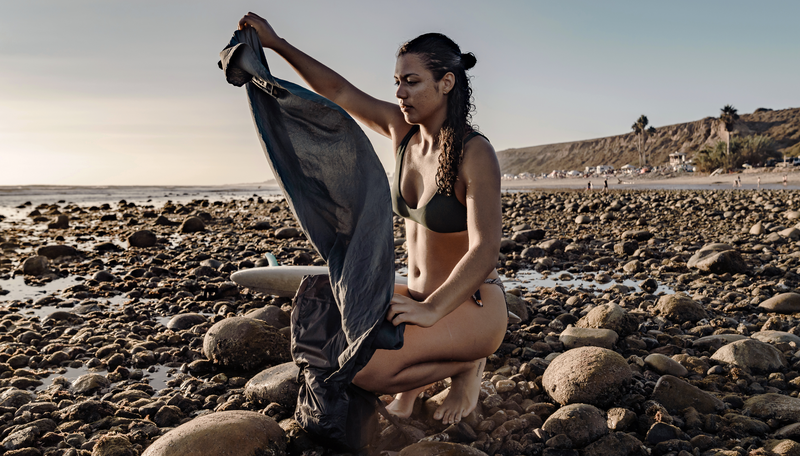 woman on rocky beach, pulling beach towel out of pocket