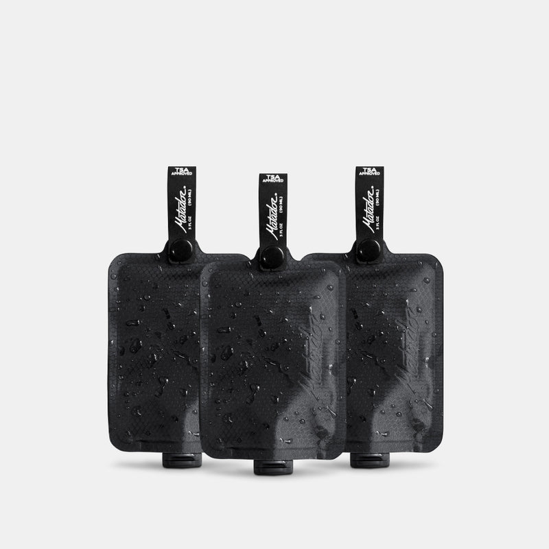 3 charcoal FlatPak Toiletry Bottles on light gray background