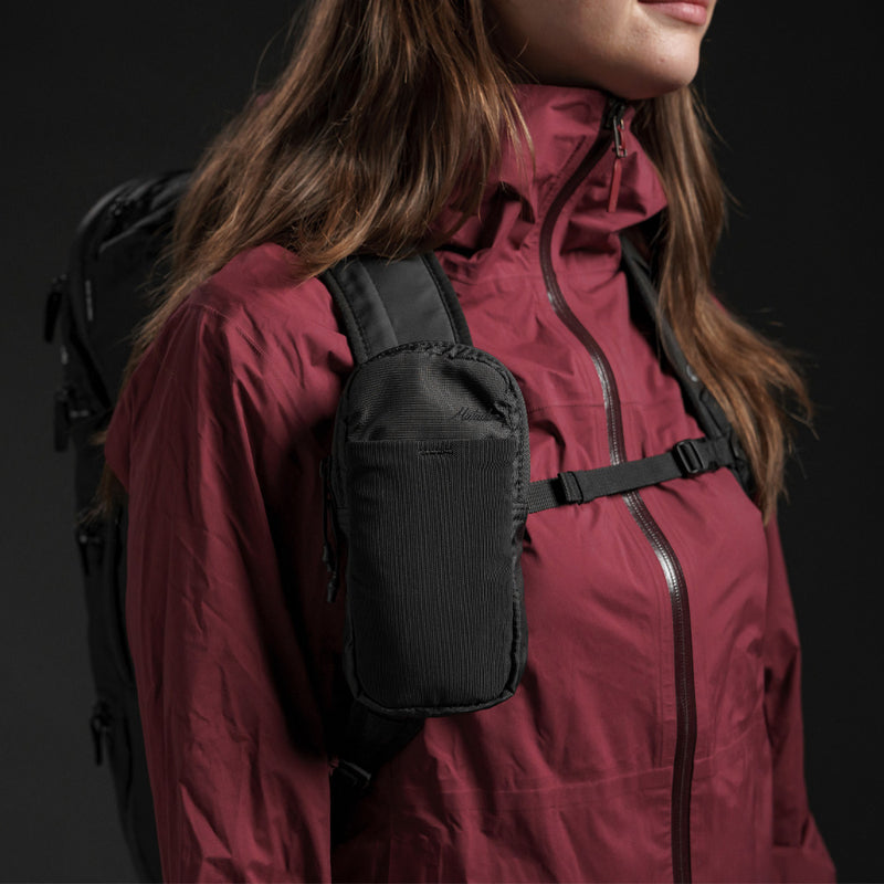 Woman in burgundy jacket, wearing speed stash on her backpack strap