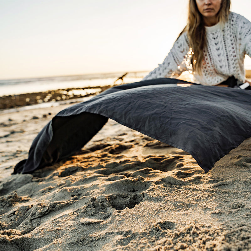 woman on sandy beach, laying out charcoal beach towel