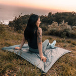 Woman sitting on Pocket Blanket overlooking a sunset ocean