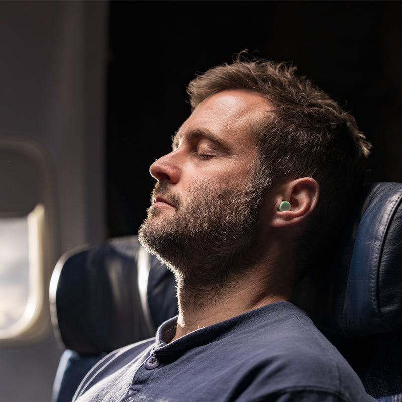 man sleeping in airplane seat, wearing mint colored ear plugs