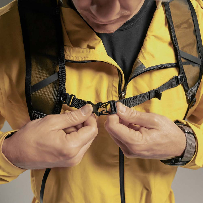 Man in yellow jacket buckling backpack sternum strap