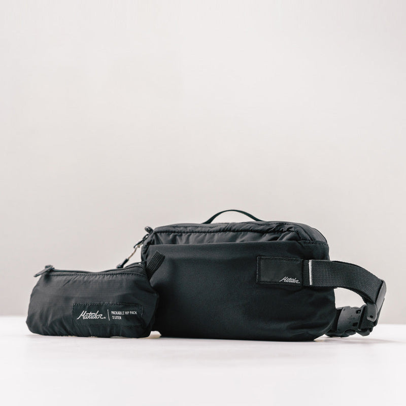 3/4 view of black sling bag and packed up bag on light gray background