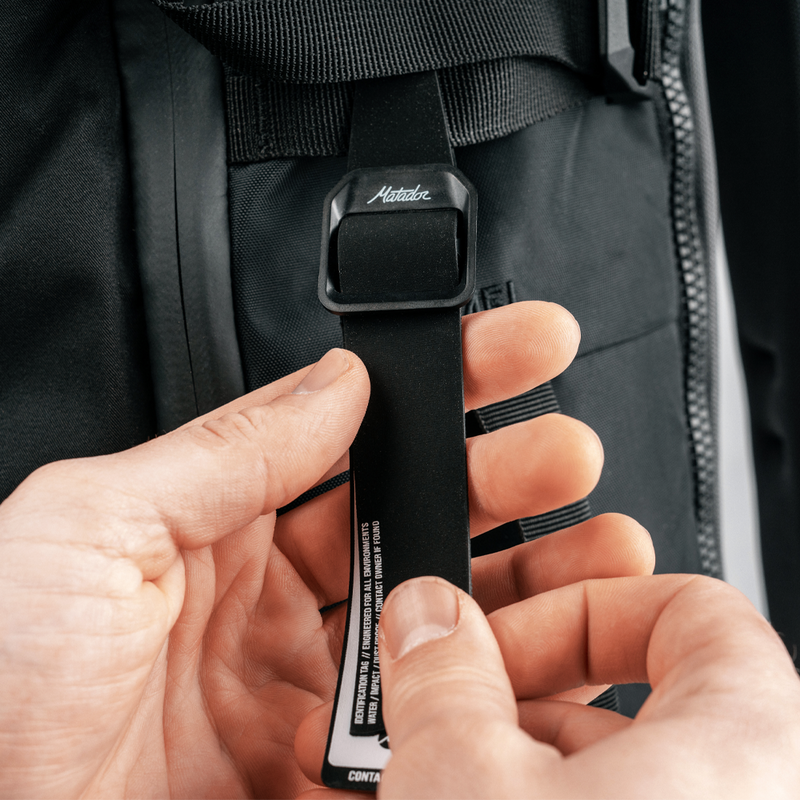 hands holding black gear tag, hanging off black backpack loop