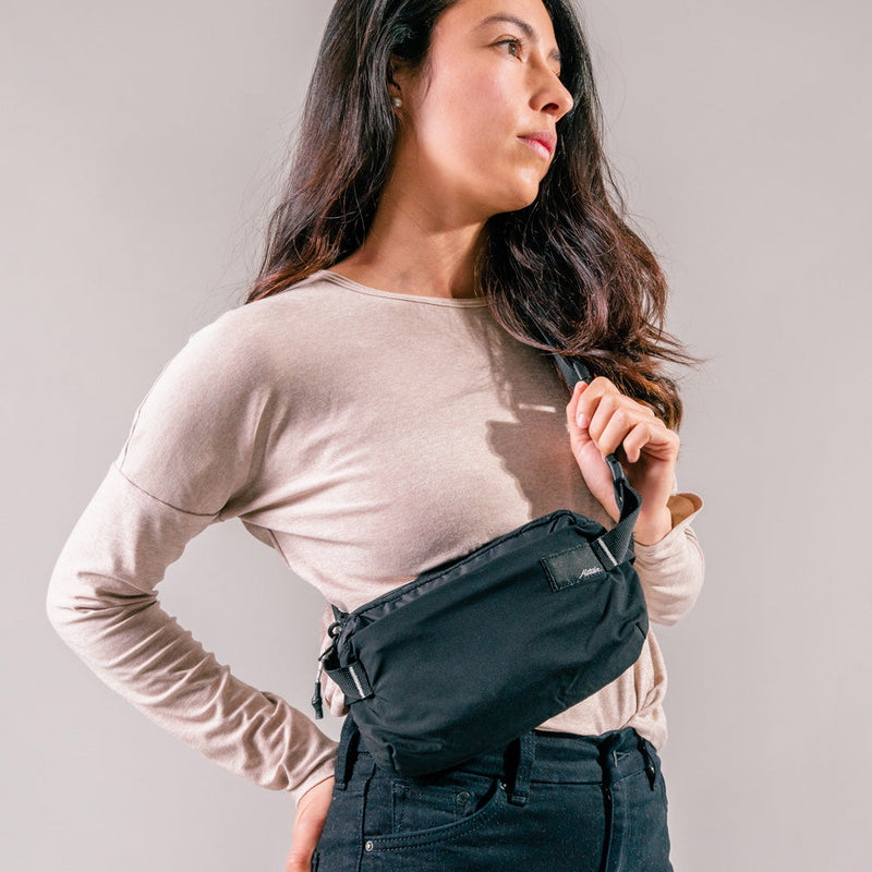 woman on light gray background wearing black sling bag across the front of her body