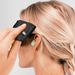 Close up view of woman wearing mint earplug, in the process of securing eyemask around her head