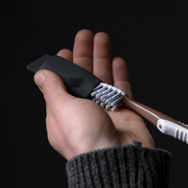 Hand pulling gold toothbrush out of charcoal toothbrush cap on black background