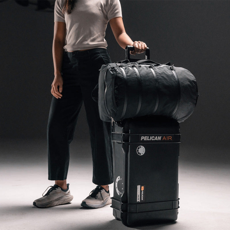 Woman on dark gray background with SEG28 sitting on top of rolling luggage
