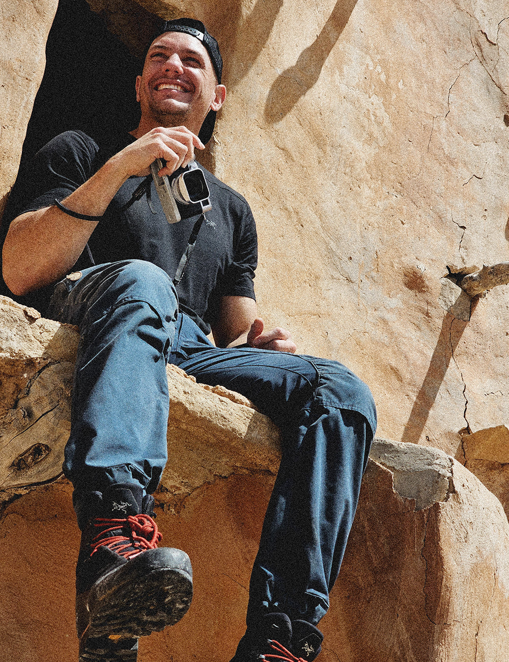 Man sitting on stone ledge holding camera and smiling