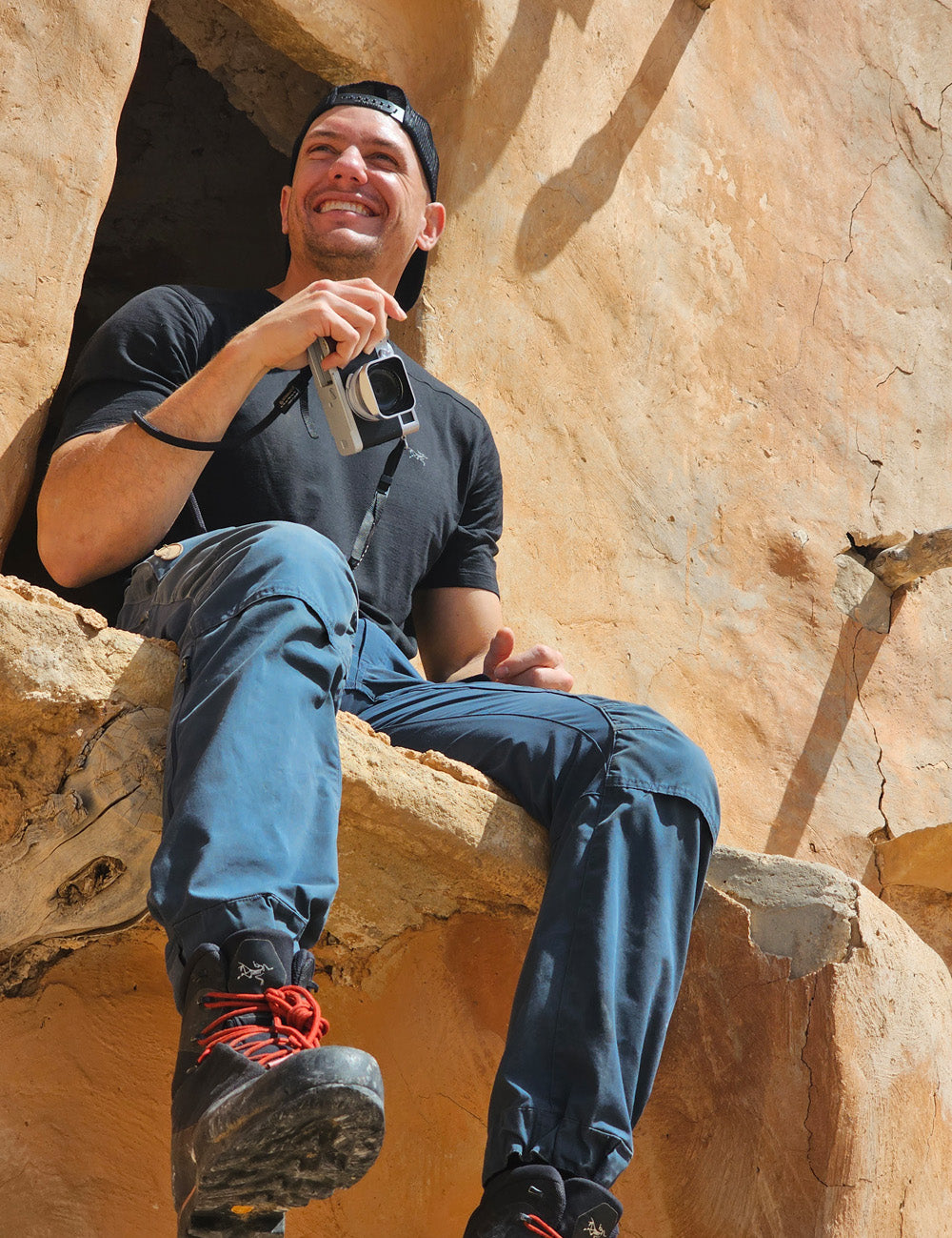 Man sitting on stone ledge holding camera and smiling