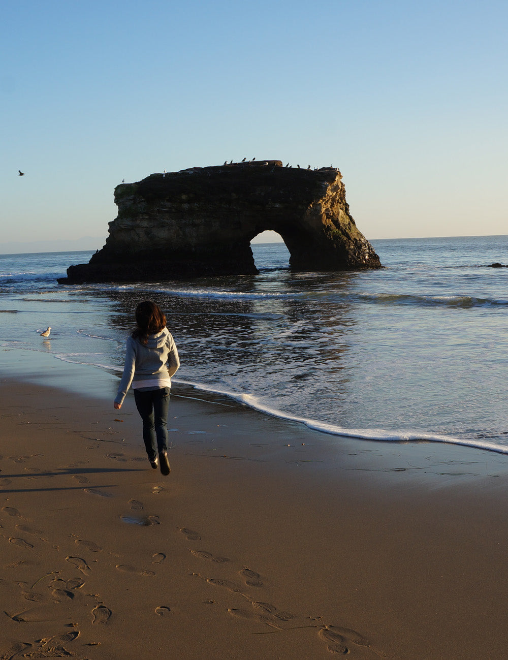 Woman running along beach with rock formations off the shore