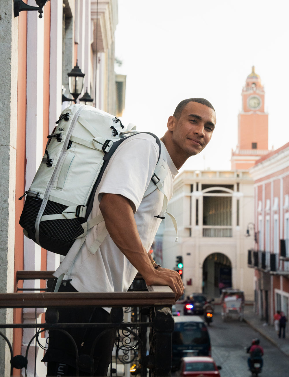 Man standing on balcony, wearing white backpack, looking out onto a pink building in Mexico