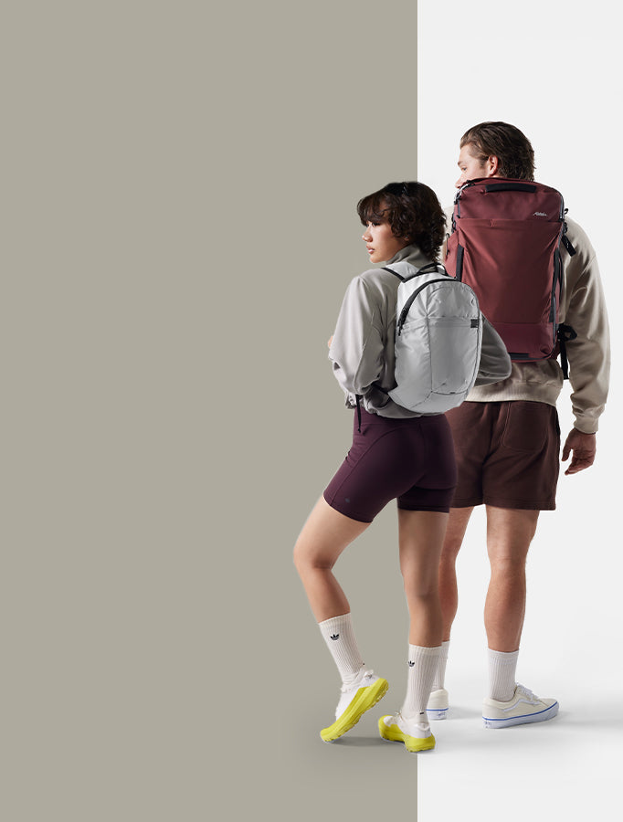 man an woman  with backpacks standing on white and beige background
