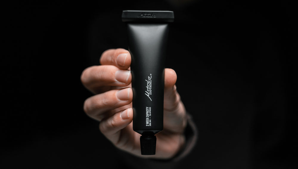 Hands on black background holding black toothpaste tube upright