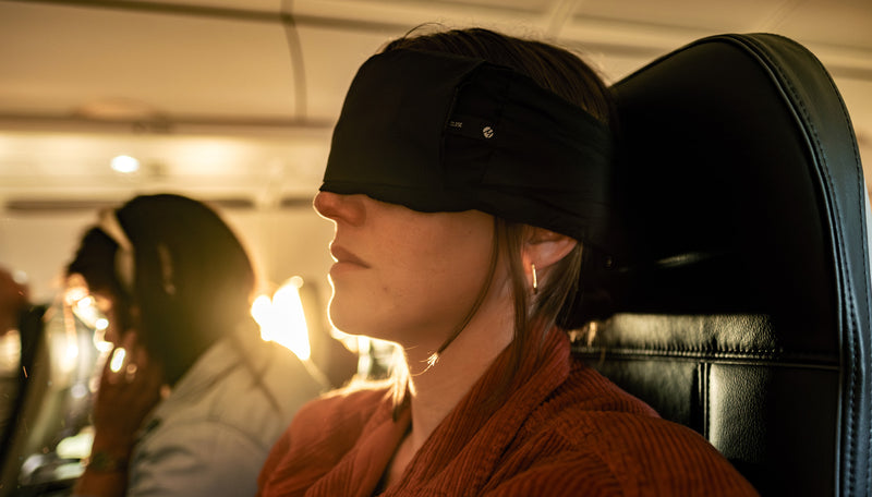 Woman sitting in sunny airplane, wearing sleep mask