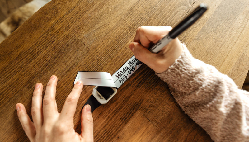 Woman's hands writing contact information onto gear tag on wooden table with a sharpie