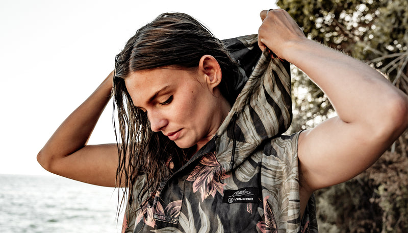 woman on rocky shoreline pulling marble floral poncho hood over her head