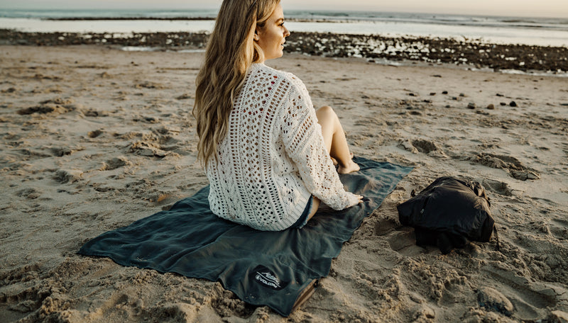 woman sitting on beach on top of charcoal beach towel