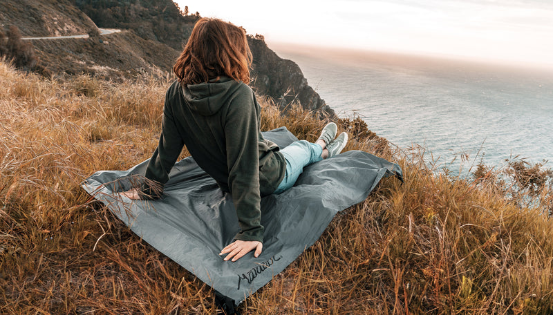 Woman sitting on a pocket blanket in a grassy cliff overlooking the ocean