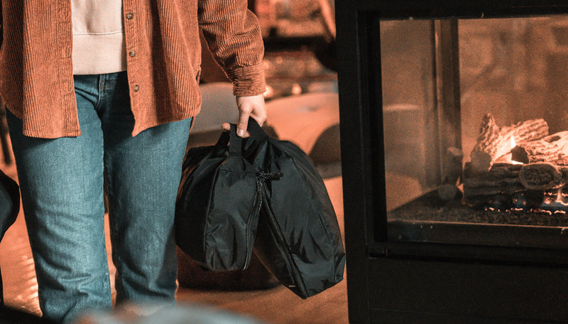 woman carrying 2 black packing cubes next to a cozy indoor fire