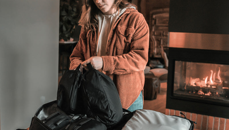 woman next to cozy indoor fire, removing black packing cube from bag