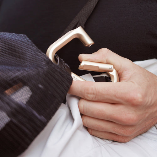 hand holding gold carabiner gate open, attaching hat to bag strap