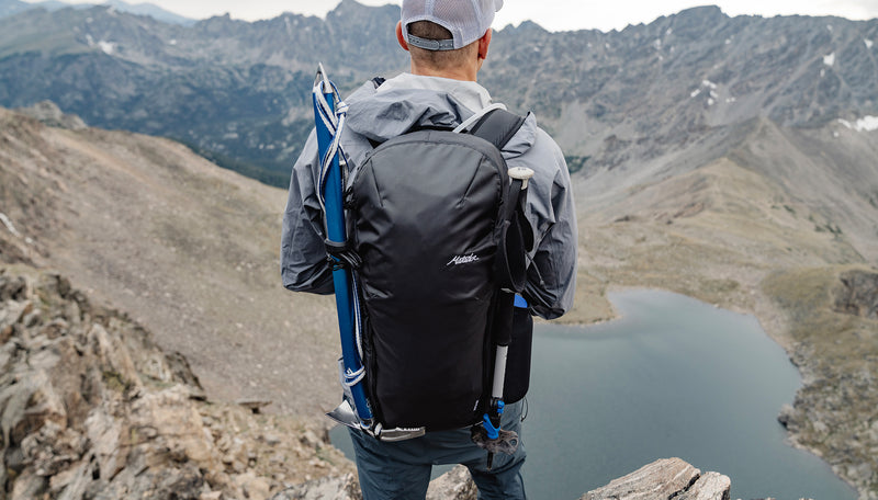 Man wearing Beast28 backpack, on top of mountain, looking down at alpine lake