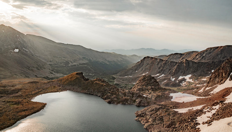 Golden hour view of alpine lake surrounded by partially snowy mountains