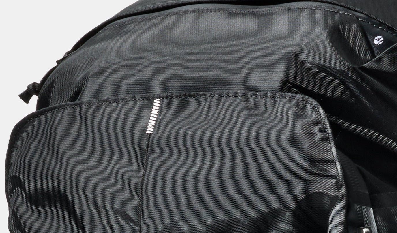 Close-up of a black nylon backpack showing the Switchback Stitch™ and fabric texture against a light gray background.