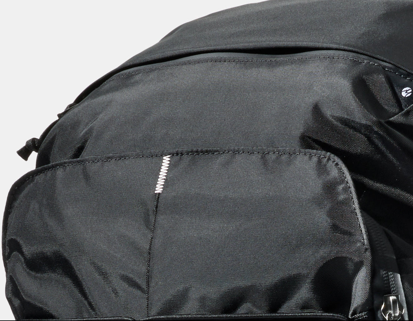 Close-up of a black nylon backpack showing the white Switchback Stitch™ on the front pocket and a small white logo on the side, against a light gray background.