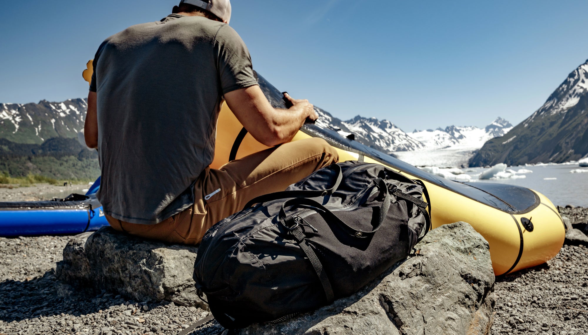 Man on shoreline with yellow, inflatable kayak with black duffle sitting next to him