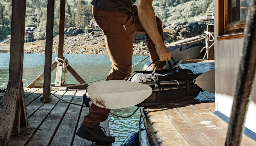 Man entering boat house carrying Freefly Duffle with Kayak paddle attached