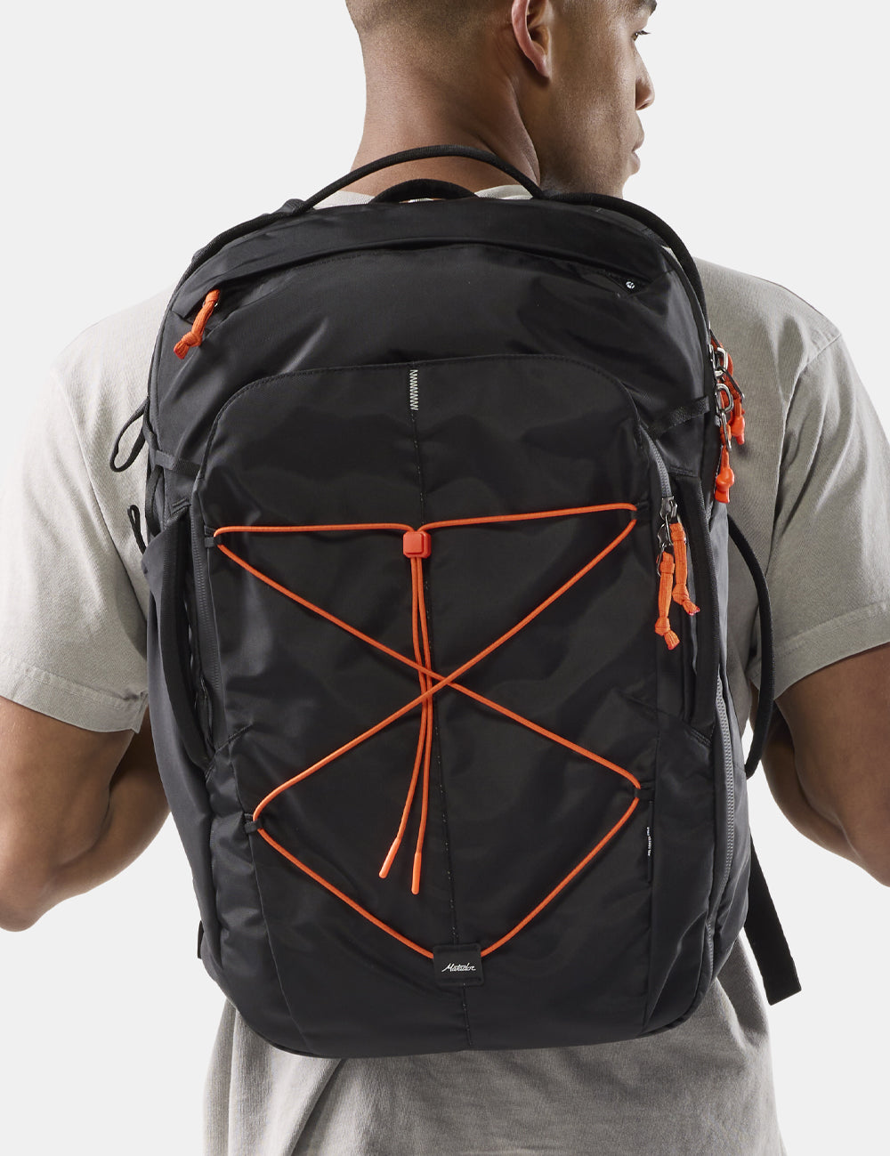 person wearing black backpack with orange cords and zipper pullers