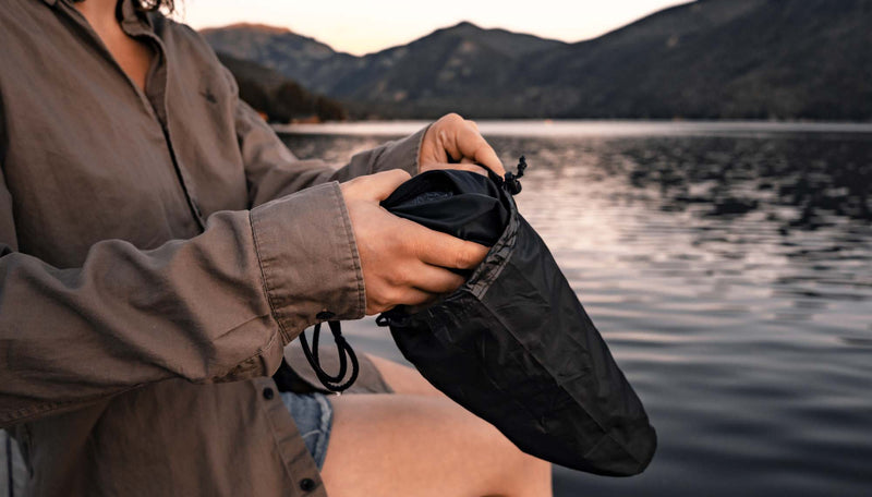 Woman sitting on dock, placing black swimsuit into black Droplet stuff sack