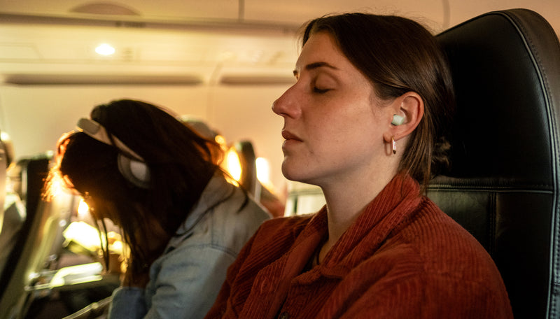Woman sleeping in sunny airplane seat, wearing mint colored ear plugs