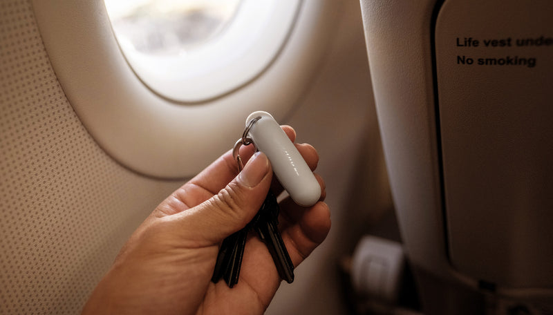 Hands holding white earplugs case attached to keys, in front of airplane window