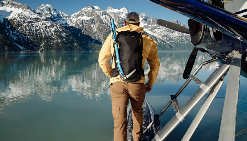 Man wearing freerain28 backpack, standing on sea plane on Alaskan lake
