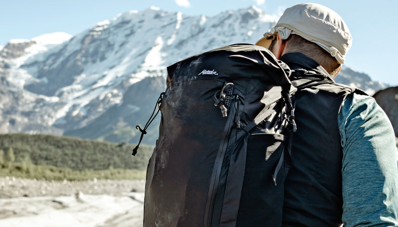 Back view of man standing in front of snowy mountain, wearing Freerain22 backpack