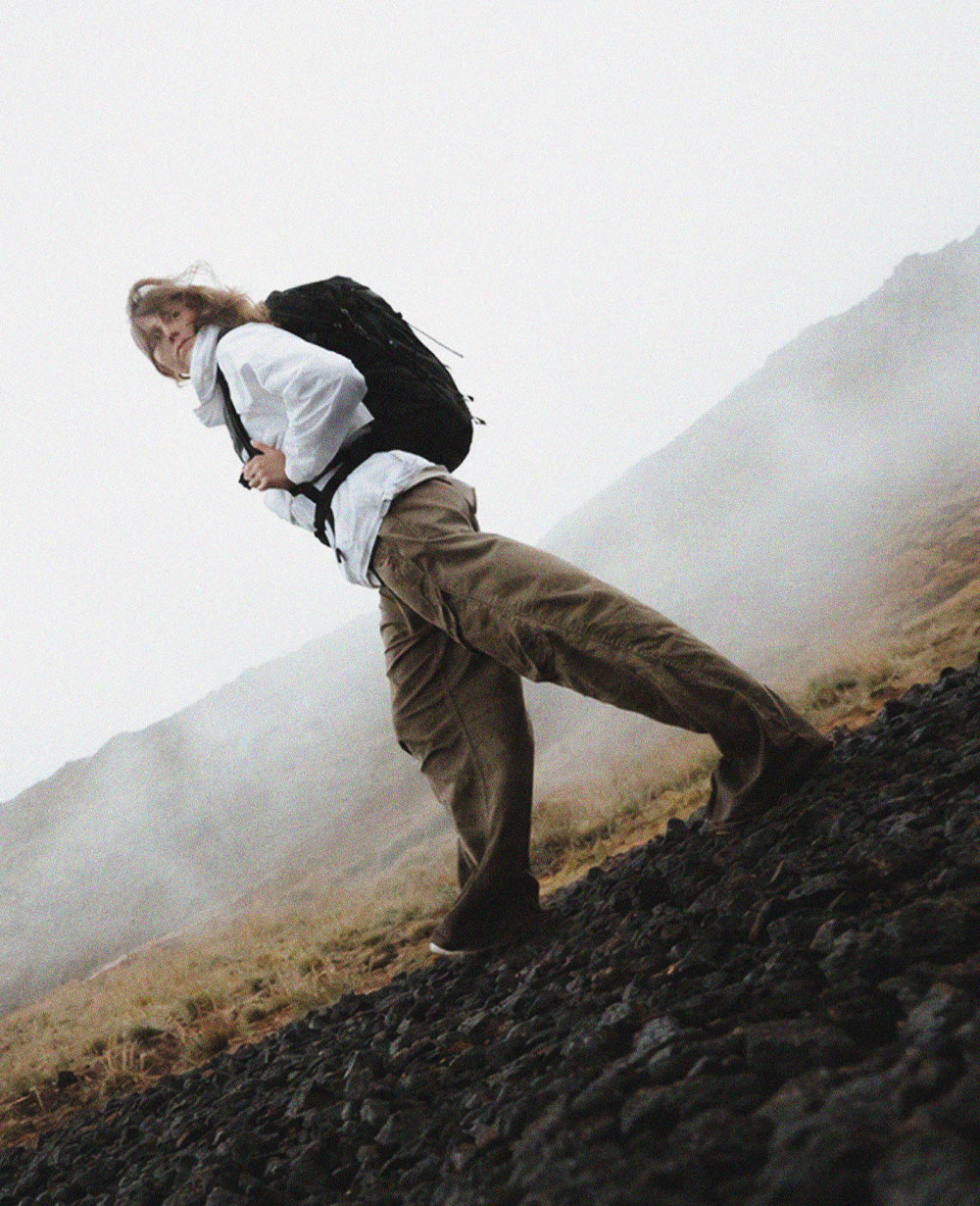 person in moody foggy setting wearing a white jacket and black backpack