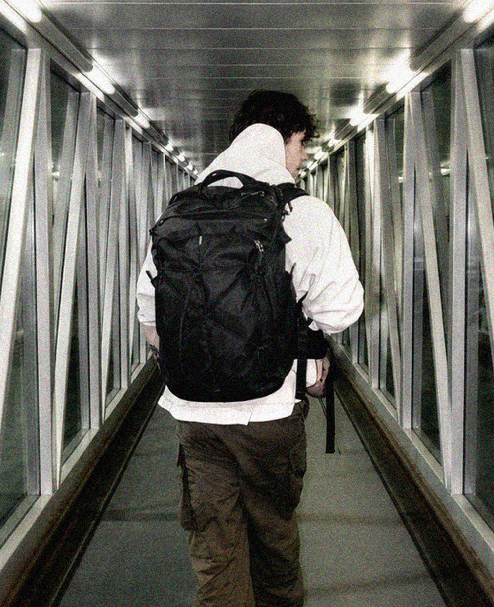 person with black backpack walking down jet bridge at night