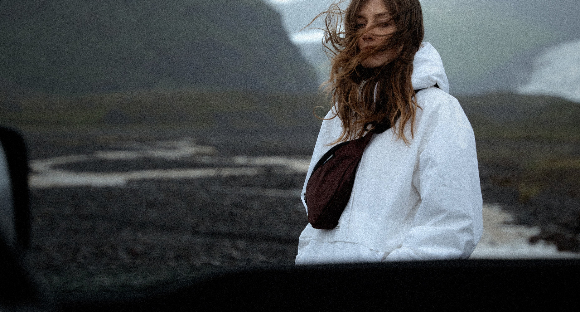 person in moody landscape wearing white jacket and garnet sling