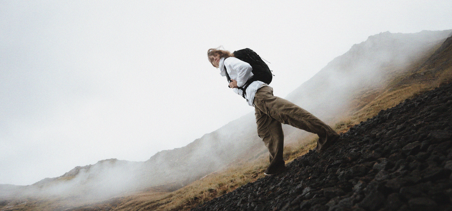 Person in white jacket and black backpack, walking through misty Icelandic setting