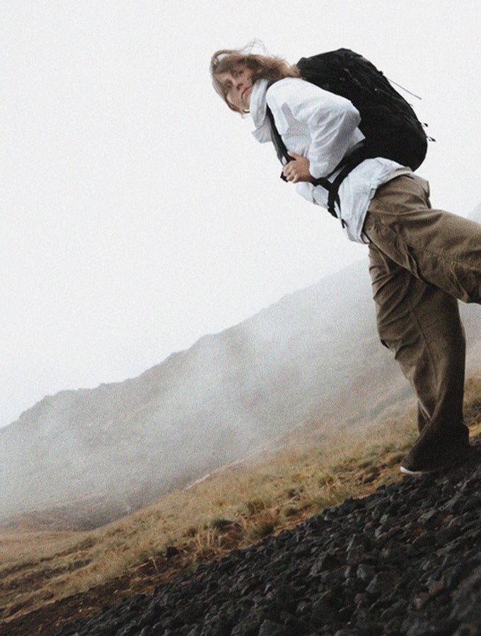 Person in white jacket and black backpack, walking through misty Icelandic setting