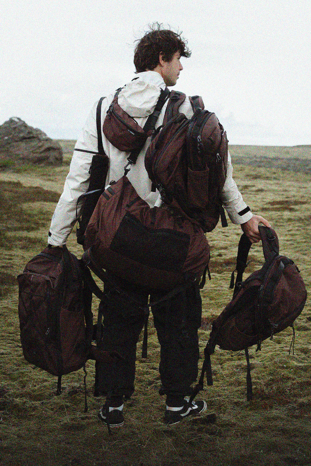 person in Icelandic landscape, wearing and holding many garnet colored bags