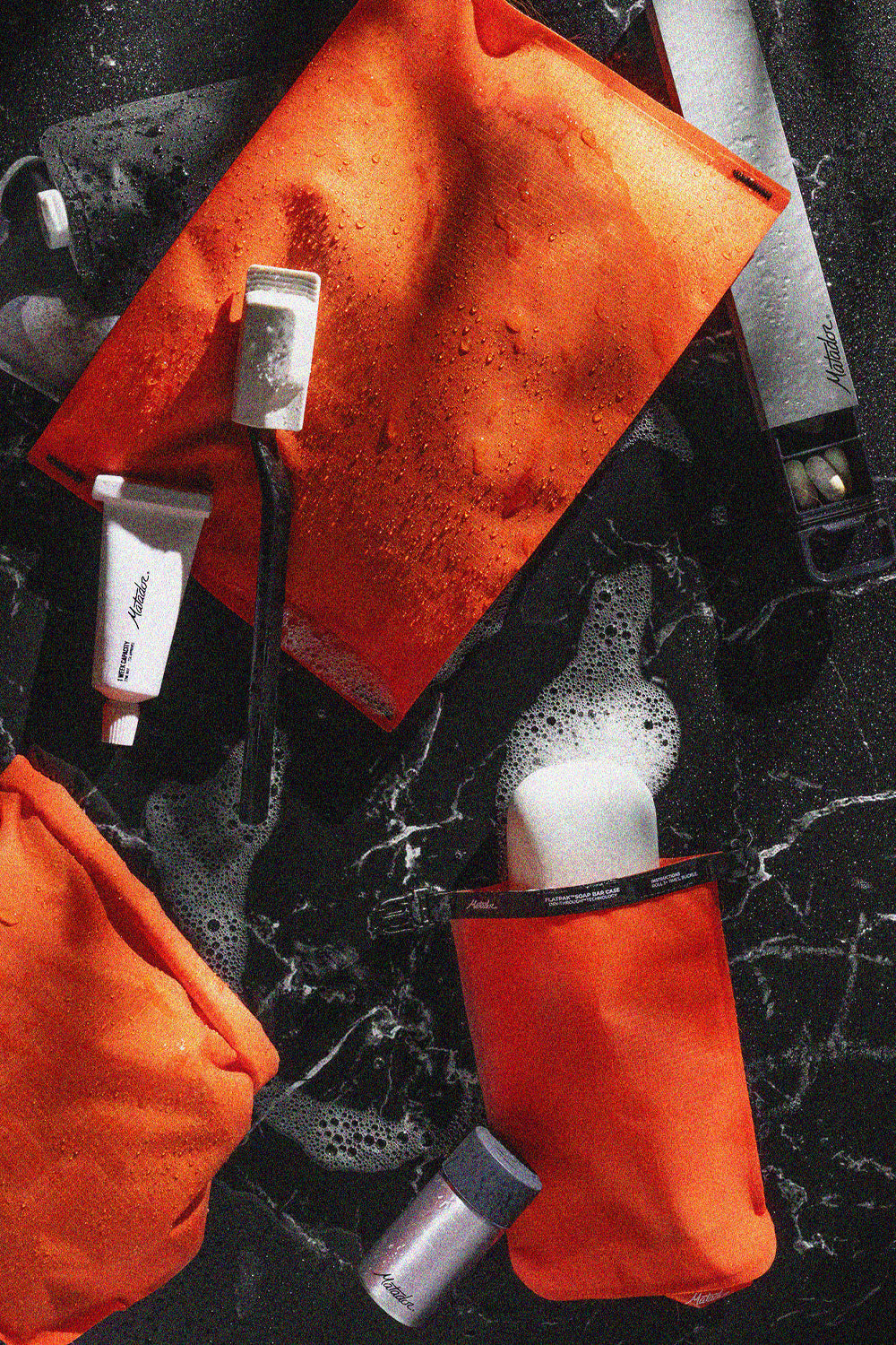 Pile of orange toiletries, soap bar, toothbrush, and pill canister on marbled black surface