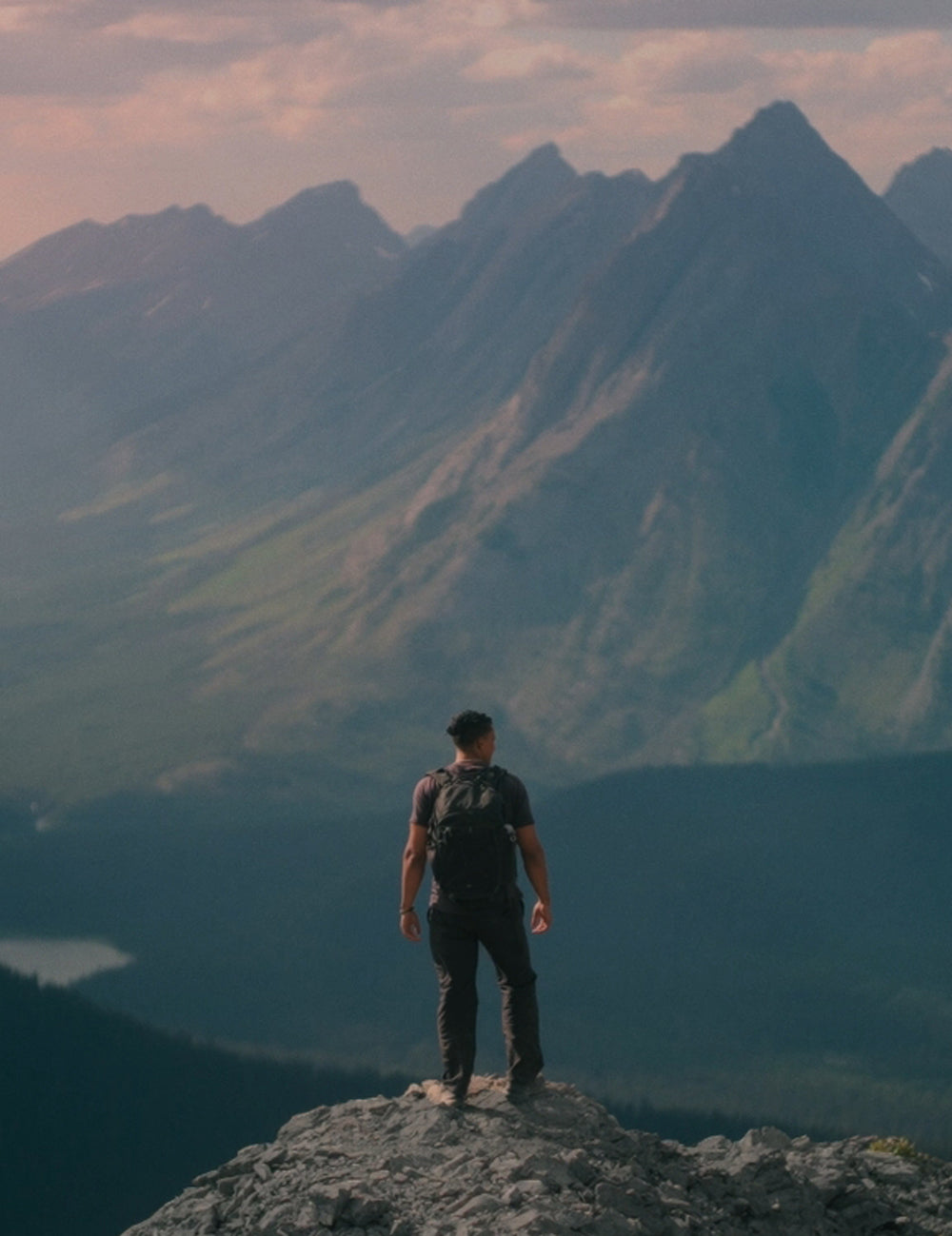 person standing on cliff in front of picturesque mountain scape