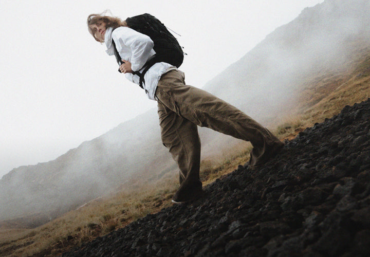Person in white jacket and black backpack, walking through misty Icelandic setting