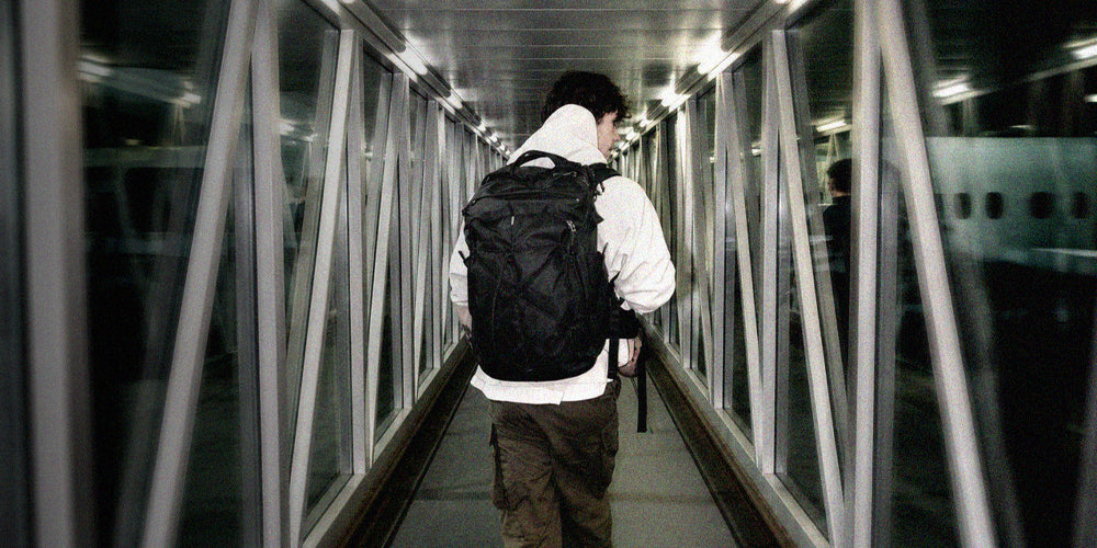 person walking down nighttime jet bridge wearing black backpack