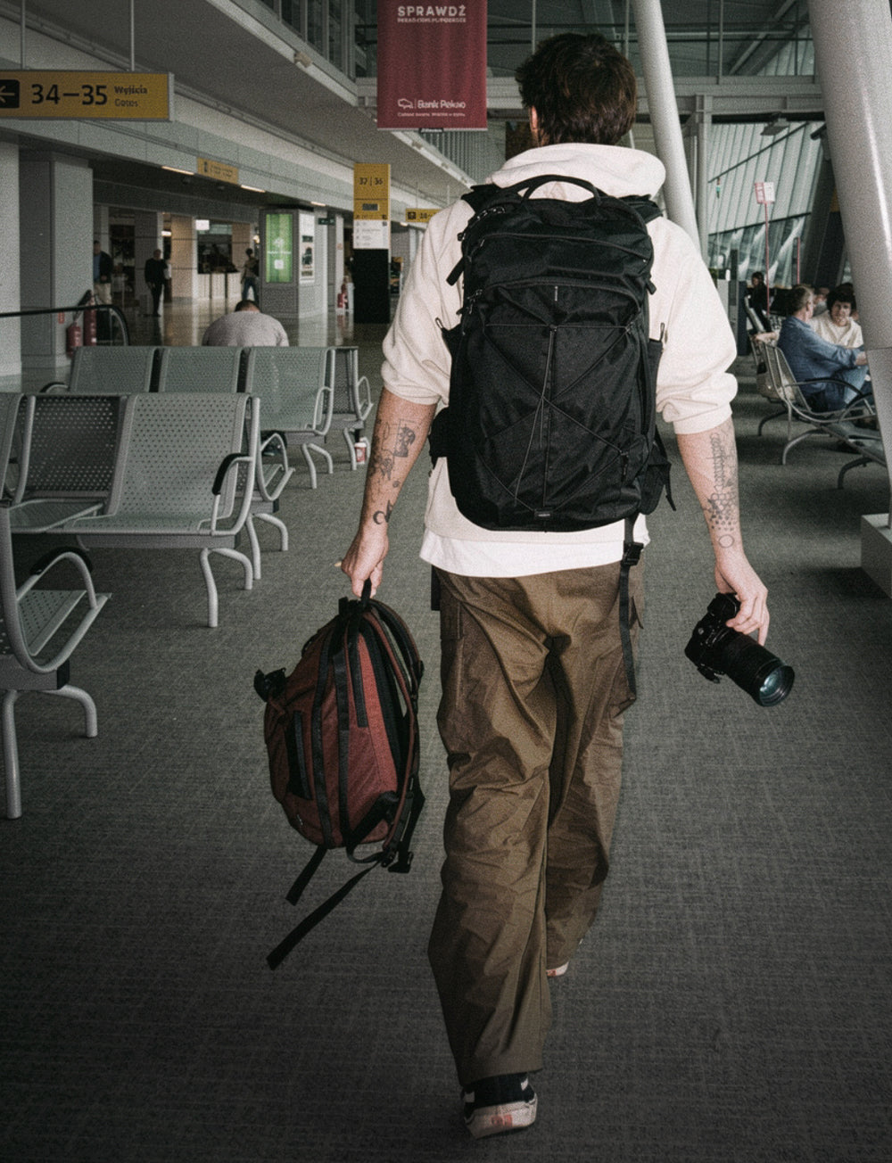 person walking through airport wearing a couple backpack and holding a camera